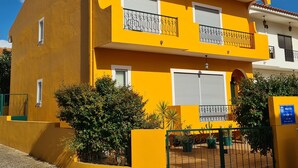 Un edificio amarillo con dos balcones, un techo de tejas y un camino de ladrillo.