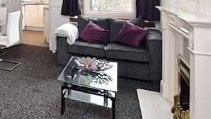 Un salon moderne avec un canapé gris, des coussins violets, une table basse en verre et une cheminée.