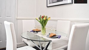 Un coin repas avec une table en verre, des chaises blanches, un vase de tulipes et un tableau encadré au mur.