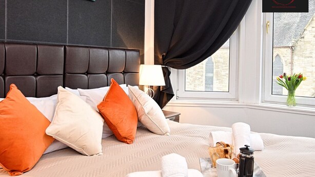 Une chambre d’hôtel avec un grand lit, plusieurs oreillers, une table de chevet avec une lampe, une fenêtre avec des rideaux et une vue sur l’extérieur.