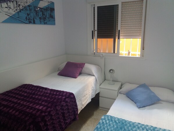 A bedroom with two beds, a nightstand, a bedside table, and a window with blinds. - TENERIFE HOLIDAY HOME (Candelaria)