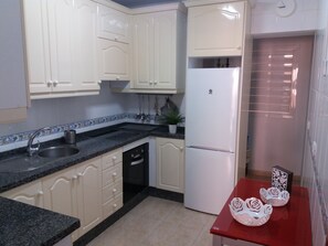 Compact kitchen with a stainless steel sink, refrigerator, and small window with blinds.