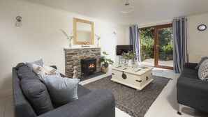 Ein Wohnzimmer mit Kamin aus Stein, grauen Sofas, einem Couchtisch und einem Fernseher.