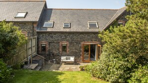 Ein Haus aus Stein mit einem geneigten Dach, einer Holztreppe, einer Bank und einem Garten.
