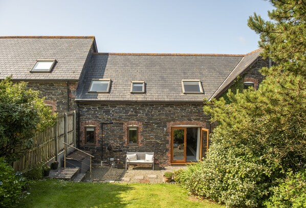 A stone house with a sloped roof, a wooden staircase, a bench, and a garden. - Curlew's Cwtch is a cosy yet contemporary three bedroom holiday home. (Wadebridge)
