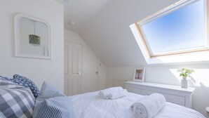 Ein Schlafzimmer mit Oberlicht, weißen Wänden und einem Bett mit aufgerollten Handtüchern.