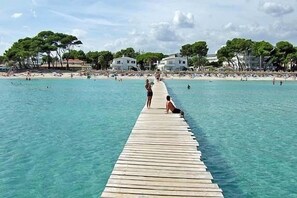 Una banchina di legno che si protende in un mare azzurro e limpido, con edifici e alberi sullo sfondo.