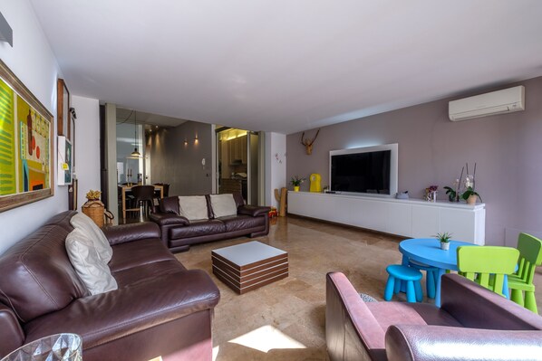 Una sala de estar moderna con un sofá de cuero marrón, una mesita de centro y un televisor sobre un mueble blanco.