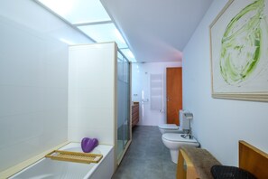 Un bagno moderno con finestra sul tetto, vasca da bagno, doccia, toilette e una panca.