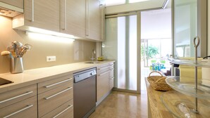 Een moderne keuken met lichte houten kastjes, een vaatwasser en een kookeiland met glazen blad.