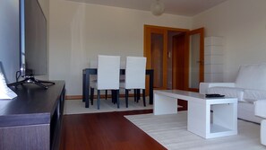 Un salon moderne avec un canapé blanc, une table à manger avec des chaises, un téléviseur posé sur un meuble et un plancher en bois.