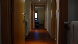 A narrow hallway with wooden flooring leading to a bedroom.