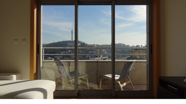 A balcony with a view of a cityscape, including a tall tower, through a sliding glass door.