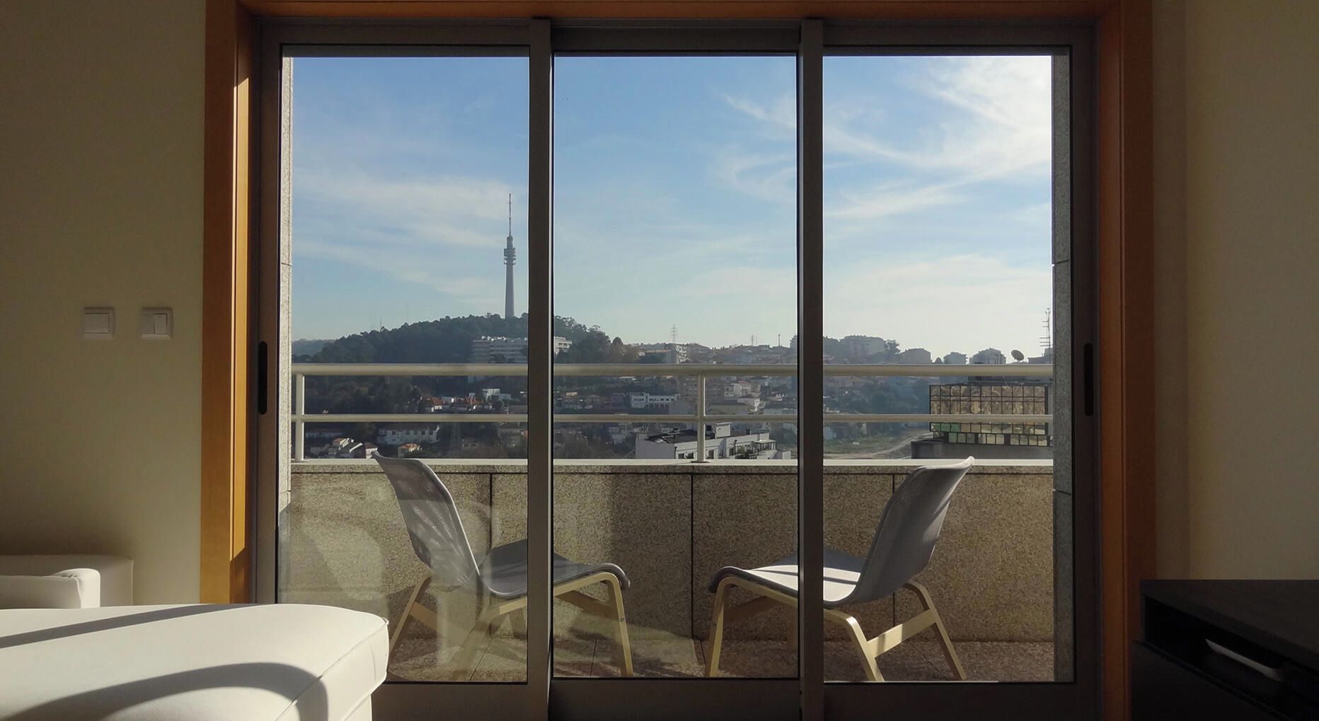 Un balcon donnant sur un paysage urbain, avec notamment une haute tour, visible à travers une porte-fenêtre coulissante.