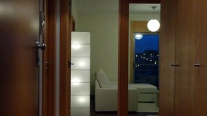 A hallway with wooden flooring leading to a bedroom with a bed and a nightstand.