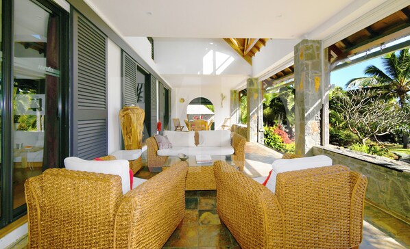 A room with wicker furniture, a white sofa, and a view of tropical vegetation. - Villa in Le Morne with pool and maid (Le Morne)