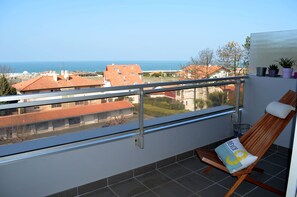 A balcony with a view of the sea, a wooden chair with a cushion, and a small potted plant. - Panoramic view of the ocean, beaches (Anglet)