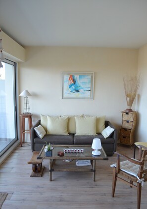 A living room with a sofa, coffee table, and a chair. There is a lamp, a picture frame, and a wicker basket. - Panoramic view of the ocean, beaches (Anglet)