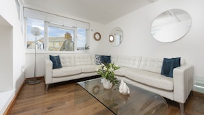 A modern living room with a sectional sofa, a glass coffee table, a potted plant, and a round mirror on the wall. - A beautiful, double-fronted terrace house situated in Port Isaac. (Port Isaac)