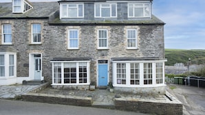 A stone building with multiple windows, a blue door, and a small porch area. - A beautiful, double-fronted terrace house situated in Port Isaac. (Port Isaac)