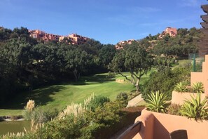 Un campo de golf con un estanque, rodeado de árboles y edificios al fondo.