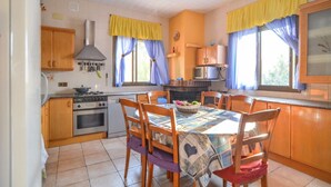 A kitchen with wooden cabinets, a stove, and a dining table with chairs. - Club Villamar - Nice lower apartment in shared villa with private fenced swimming pool, small gym... (Macanet de la selva)