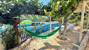 A pool area with a hammock, stone flooring, and a blue fence. - Club Villamar - Nice lower apartment in shared villa with private fenced swimming pool, small gym... (Macanet de la selva)