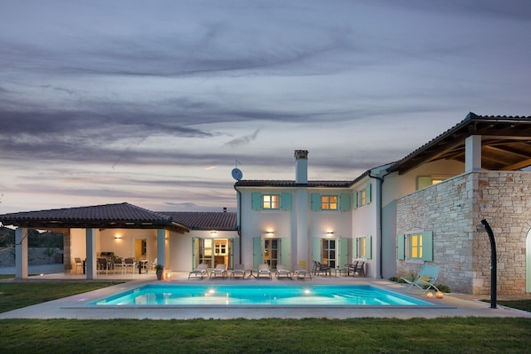 A two-story house with a swimming pool, outdoor seating, and a stone wall.