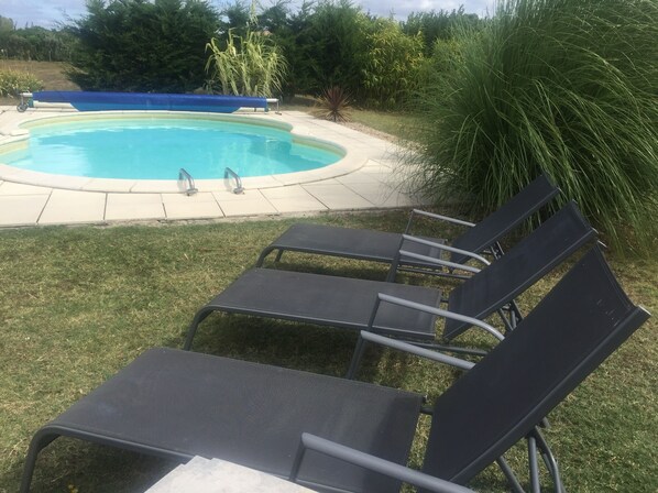 A swimming pool with a blue cover, surrounded by a concrete deck. There are three black lounge chairs with metal frames.