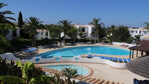 A resort pool area with multiple lounge chairs and umbrellas, surrounded by palm trees and buildings. - Lovely Spacious Apartment Facing South With Sea Views with use of  communal pool (Sesmarias)