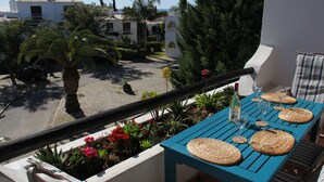 A balcony with a table set for dining, overlooking a street with parked cars and buildings. - Lovely Spacious Apartment Facing South With Sea Views with use of  communal pool (Sesmarias)