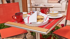 A dining table with a tray of pastries, a red mug, and a bowl with a yellow lid.