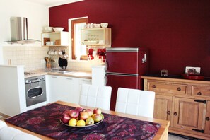 A kitchen with white cabinets, a red refrigerator, and a dining table with a fruit bowl.