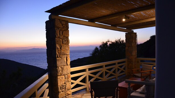 A stone balcony with a wooden railing overlooking a coastal view at sunset.