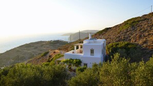 A white building with a flat roof and satellite dish, surrounded by greenery and overlooking a coastal landscape.