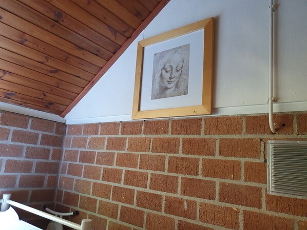 A bathroom with a wooden ceiling, a brick wall, and a framed drawing on the wall.