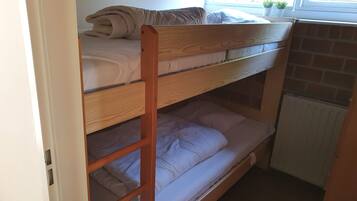 A bunk bed with a wooden frame, a window with a view of greenery, and a radiator below the lower bunk.