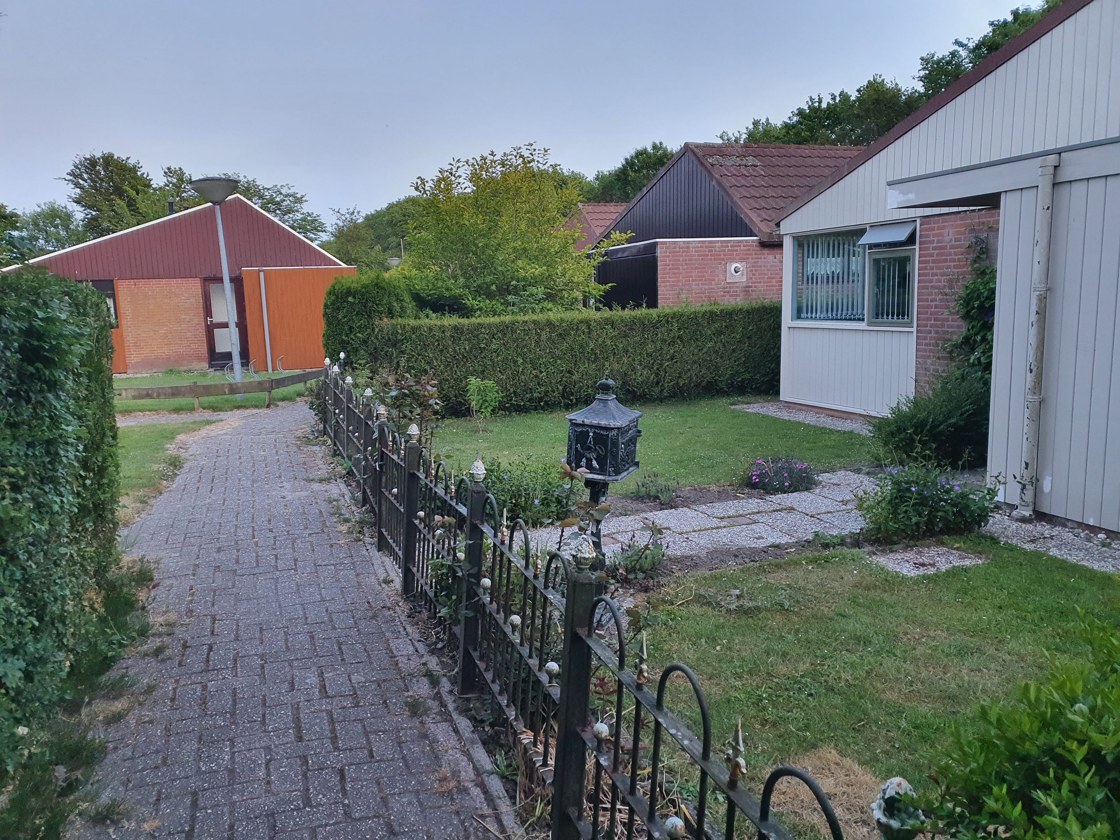 Un chemin pavé mène à une zone délimitée par une grille et agrémentée d’une lanterne décorative.