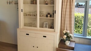 Una habitación con techo de madera, un armario blanco con puertas de vidrio y una ventana con cortinas.