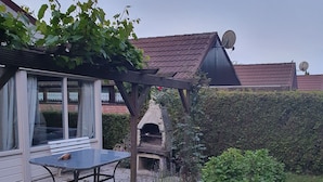 Un patio con mesa y sillas, un horno de ladrillo y una pérgola con plantas trepadoras.