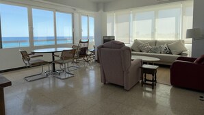 A spacious living room with a large window overlooking the sea, a sofa, a red armchair, and a dining area with chairs. - Beautiful sea view from all rooms, communal swimming pool / tennis (El Campello)