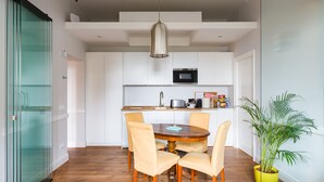 A compact kitchen with white cabinets, a microwave, and a sink. There is a dining table with four chairs and a potted plant.