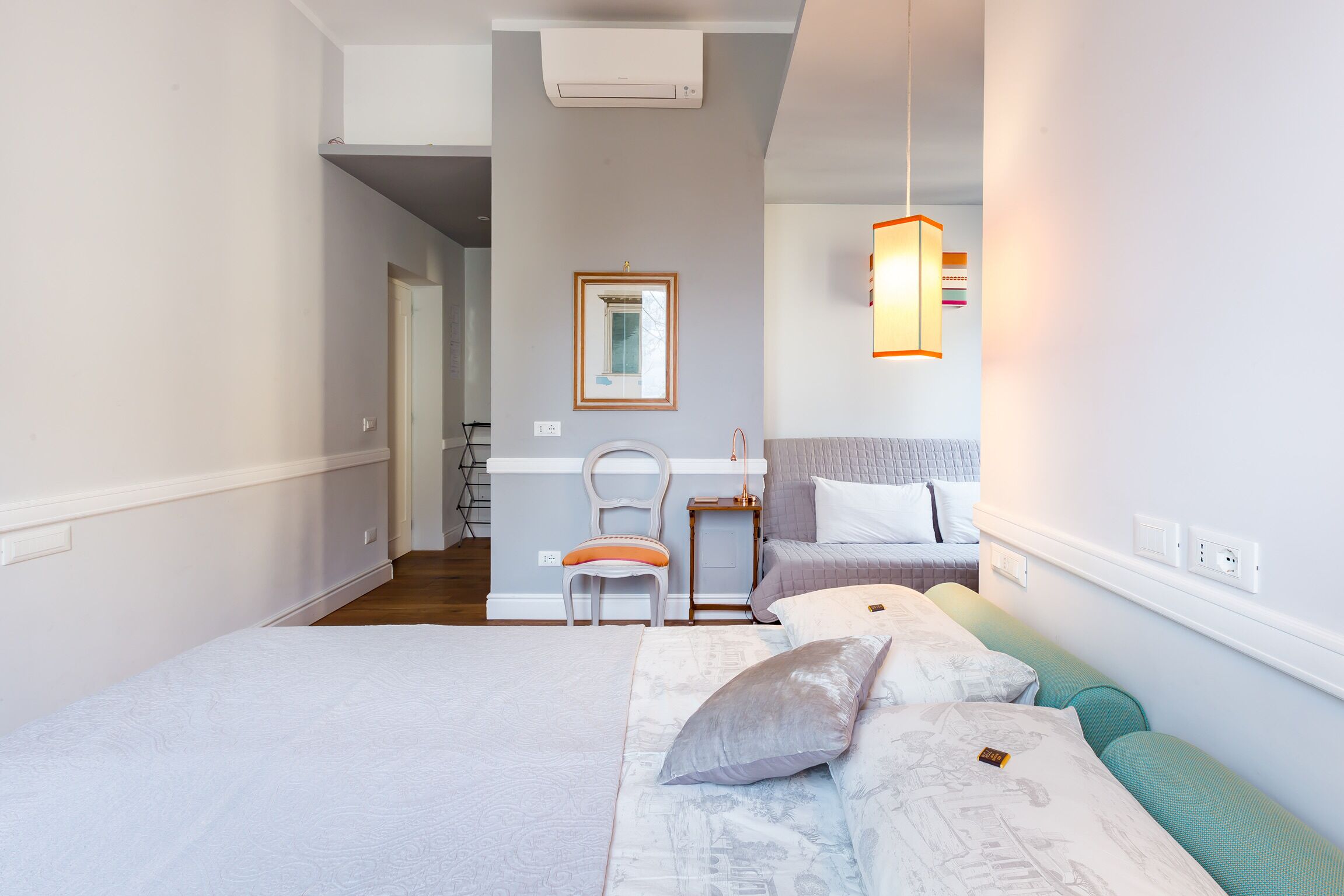 Un dormitorio con cama, una silla, una mesita de noche y una lámpara colgante.