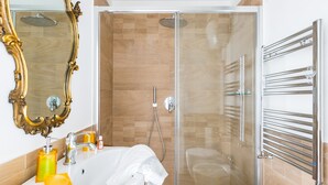 A modern bathroom with a glass-enclosed shower, a white sink with a gold faucet, and a large ornate mirror.