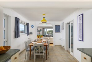 A dining area with a table set for four, chairs, a vase with sunflowers, and a view into the living room. - Palm Trees is located in a quiet setting to the rear of Westwood Flats. (Wadebridge)