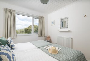 Ein Schlafzimmer mit zwei Betten, einem fensterbelaubten Fenster, einem Heizkörper, einem Spiegel und einem Teddybären.
