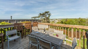 Una terraza de madera con una mesa dispuesta para comer, rodeada de sillas, con vistas a un paisaje pintoresco.