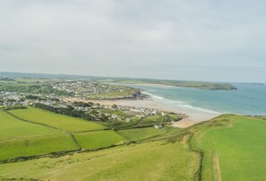 An aerial view of a coastal town with green fields, a beach, and houses.