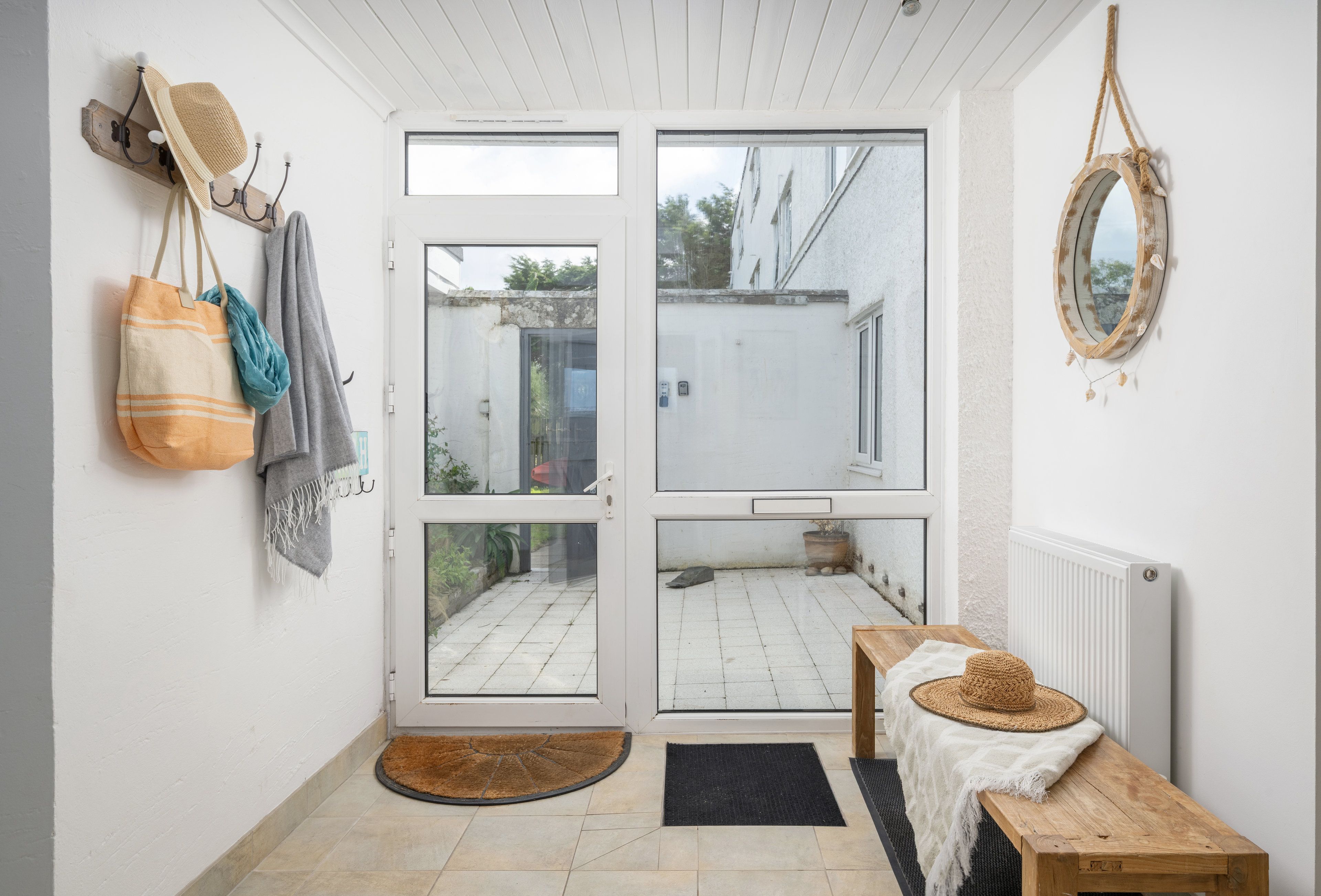 Une pièce dotée d’une porte-fenêtre coulissante donnant sur un espace extérieur, d’un banc en bois, d’un panier en osier et d’un miroir fixé au mur.