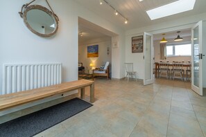 A spacious living area with a wooden bench, a round mirror, and a view into the kitchen.